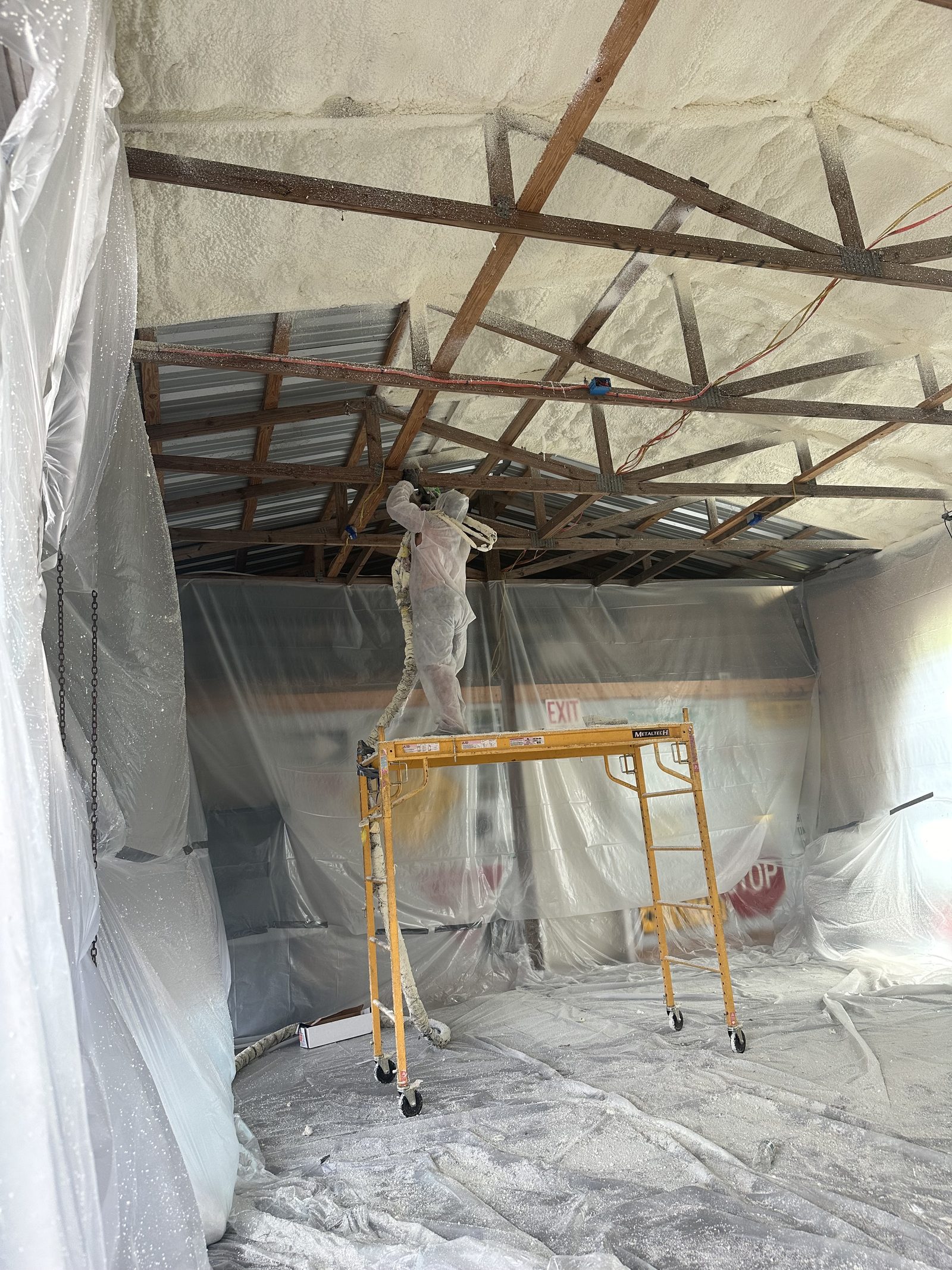Insulflo installer spraying foam insulation from scaffolding during a commercial job